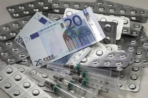 Euro banknotes, medical high blood pressure pills in foil, medical syringes. Euro cash,  money for the health care and purchase of pills and drugs.
