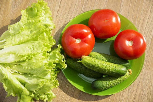 Fresh vegetables. Tomato, cucumber and lettuce leaves on a green plate. — Stock Photo, Image