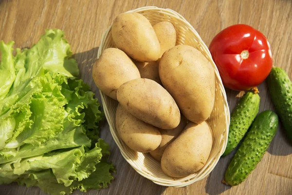 Fresh vegetables. Tomatoes, cucumbers and lettuce on a wooden table. Potatoes in a wicker basket. — Stock Photo, Image