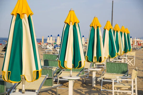 Tarde en la playa en verano En Rímini, Italia. Líneas de sombrillas cerradas y tumbonas en una playa vacía . — Foto de Stock