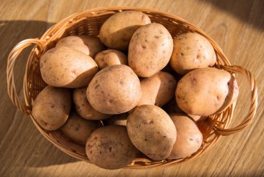 Ahşap bir masa üzerinde bir hasır sepet içinde taze patates.