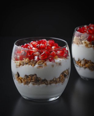 Yoğurt, granola ve nar meyveleri siyah tahta bir masada cam bir bardakta. Lezzetli tatlı Sağlıklı kahvaltı
