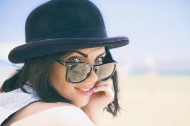 Siyah şapka ve sahilde retro güneş gözlüğü gülümseyen güzel genç kadın portresi