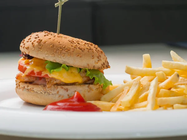 Big burger with french fries and ketchup on white plate