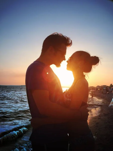 Belo jovem casal olhando uns para os outros ao pôr do sol na praia do oceano — Fotografia de Stock
