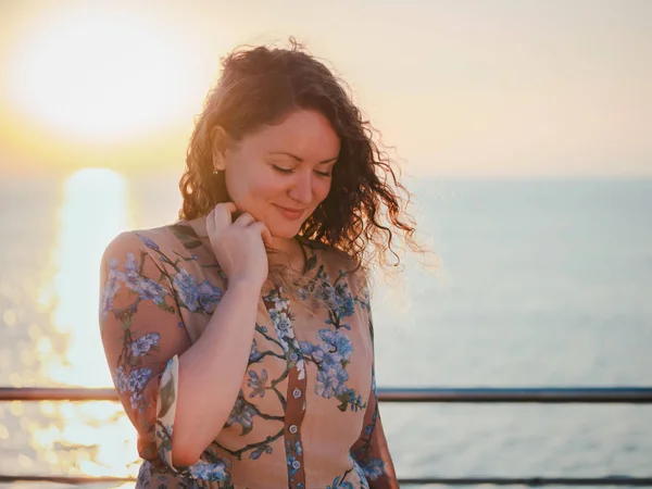 Портрет молодої красивої жінки з кучерявим світлим волоссям, що стоїть біля моря або океану на сході сонця — стокове фото