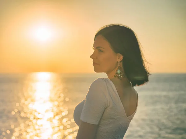 Портрет молодой привлекательной женщины, стоящей в утреннем солнечном свете у моря или океана. Красивая женщина с короткими брюнетками и длинными серьгами . — стоковое фото