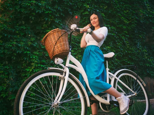 美丽年轻有魅力的女人站在白色复古自行车绿色叶子背景墙附近. — 图库照片