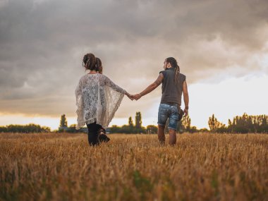 bir siyah adam bez ve dreadlocks ile uzun elbiseli hamile bir kadın tutulur elinde, mavi gökyüzü, doğa, sonbahar veya yaz sezonu arka planı. aşk hikayesi. Dövme ile resmi olmayan insanlar