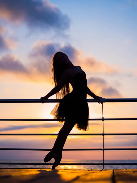 Sylwetka taniec baleriny w tutu balet czarny i pointe na skarpie nad morze na wschód lub zachód słońca lub ocean. Młoda atrakcyjna kobieta blondynka z długimi włosami, ćwiczenia, rozciąganie i ćwiczenia. — Zdjęcie stockowe