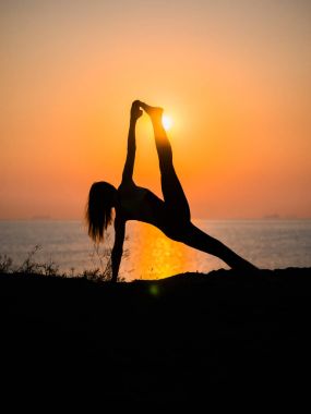 Siluet genç kadın şaşırtıcı gün batımında sahilde deniz üzerinde Yoga uygulamak. Fitness, spor, yoga ve sağlıklı yaşam konsepti.