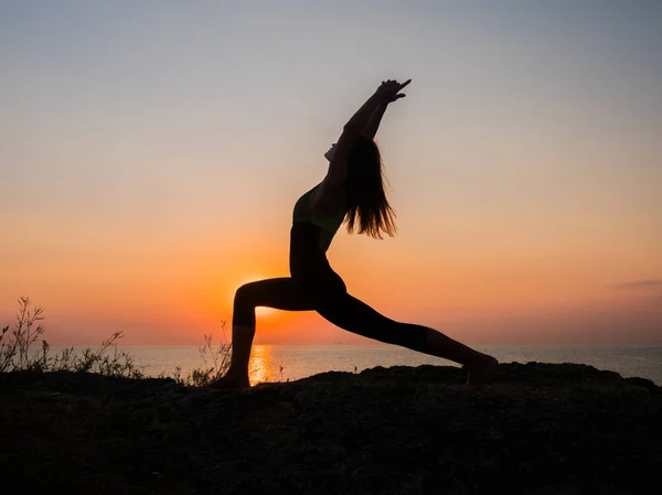 Силует молода жінка практикує йогу на пляжі над морем на дивовижному заході сонця. фітнес, спорт, йога та концепція здорового способу життя . — стокове фото