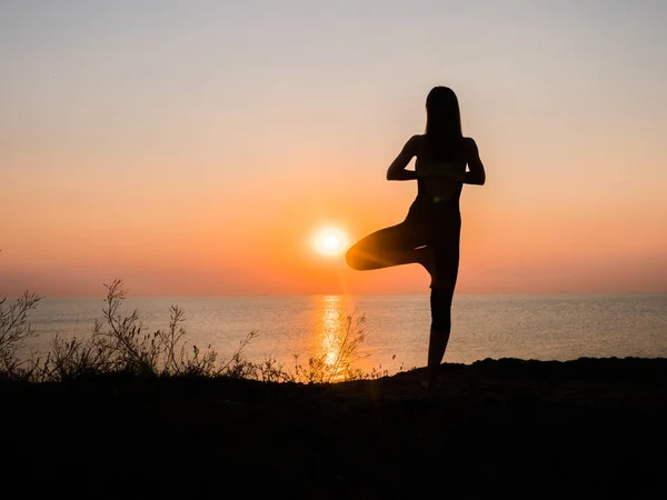 Silhouette giovane donna che pratica yoga sulla spiaggia sopra il mare al tramonto sorprendente. fitness, sport, yoga e stile di vita sano . — Foto Stock