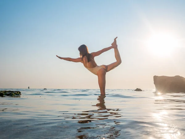 Mujer joven caucásica en traje de baño practicando yoga en el mar de agua o en el océano. Hermoso reflejo. Asanas complejas, equilibrio. Fitness, deporte, yoga y estilo de vida saludable . — Foto de Stock