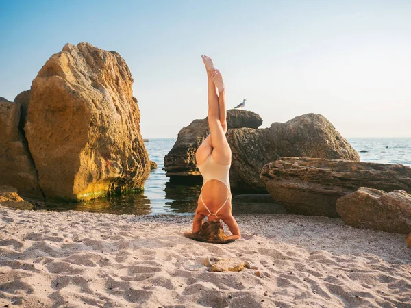 Mulher caucasiana jovem em maiô praticando ioga na areia na natureza. Alongamento, equilíbrio, asana duro. Fitness, esporte, ioga e conceito de estilo de vida saudável. Shirshasana, Cabeceira . — Fotografia de Stock