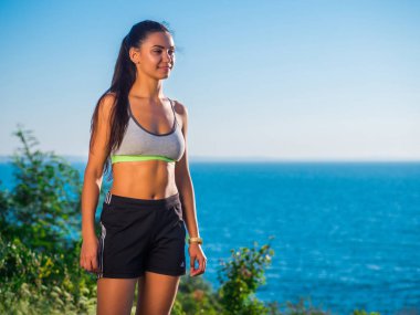 Genç aktif sportif başarılı kadın ayakta deniz ya da okyanus üstünde yüksek tepede. Spor giyim güzel kız. Sağlık kavramı.