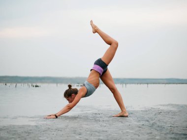 Sağlıklı yaşam egzersiz kavramı - genç sportif uygun kadın yoga Sun salutation Surya Namaskar poz Hasta Uttanasana sahilde sunset bulvarında yaparken.