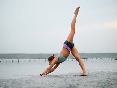 Sağlıklı yaşam egzersiz kavramı - genç sportif uygun kadın yoga Sun salutation Surya Namaskar poz Hasta Uttanasana sahilde sunset bulvarında yaparken.