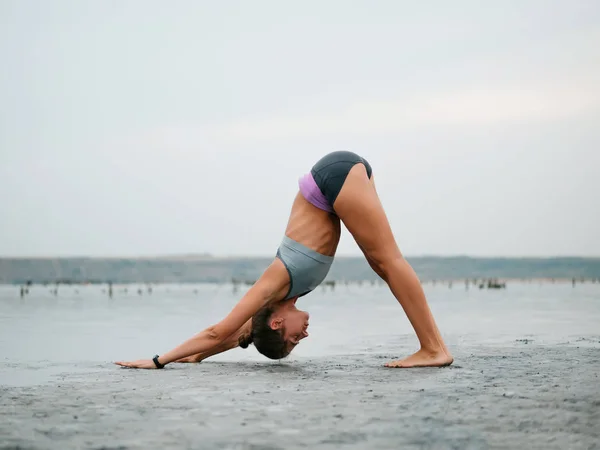 Concepto de ejercicio de vida saludable - Mujer joven en forma deportiva haciendo yoga Saludo al sol Surya Namaskar pose Hasta Uttanasana en la playa al atardecer . — Foto de Stock