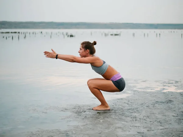 Conceito de exercício de vida saudável - Jovem mulher sporty fit fazendo ioga Saudação ao sol Surya Namaskar pose Hasta Uttanasana na praia no pôr do sol . — Fotografia de Stock
