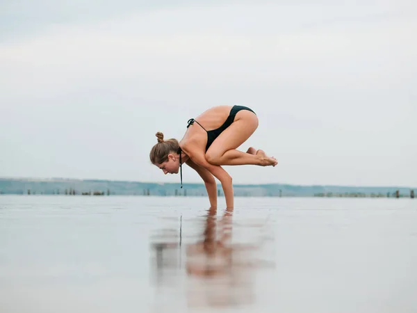 Mulher caucasiana jovem em maiô praticando ioga em água liman, lago ou rio. Belo reflexo. Asanas complexas, equilíbrio. Fitness, esporte, ioga e conceito de estilo de vida saudável . — Fotografia de Stock