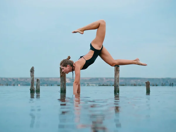 Joven mujer caucásica en traje de baño practicando yoga en agua liman, lago o río. Hermoso reflejo. Asanas complejas, equilibrio. Fitness, deporte, yoga y estilo de vida saludable . — Foto de Stock