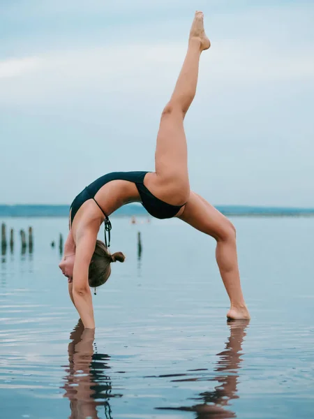 Mulher caucasiana jovem em maiô praticando ioga em água liman, lago ou rio. Belo reflexo. Asanas complexas, equilíbrio. Fitness, esporte, ioga e conceito de estilo de vida saudável . — Fotografia de Stock