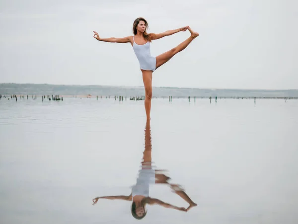 Joven mujer caucásica en traje de baño practicando yoga en agua liman, lago o río. Hermoso reflejo. Asanas complejas, equilibrio. Fitness, deporte, yoga y estilo de vida saludable . — Foto de Stock