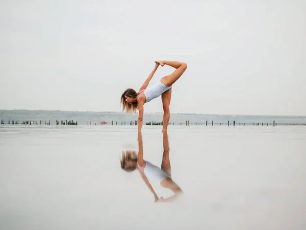 Mulher caucasiana jovem em maiô praticando ioga em água liman, lago ou rio. Belo reflexo. Asanas complexas, equilíbrio. Fitness, esporte, ioga e conceito de estilo de vida saudável . — Fotografia de Stock