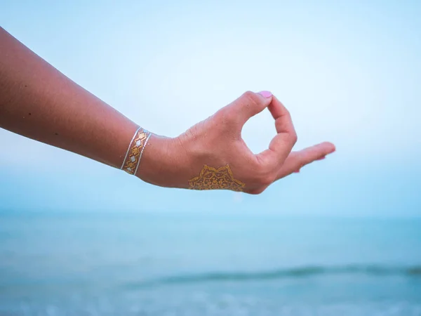 Ezüst és arany flash tetoválás a női átadja a tenger, vagy óceán háttér. Nő gyakorló jóga. Gyan Kata. — Stock Fotó