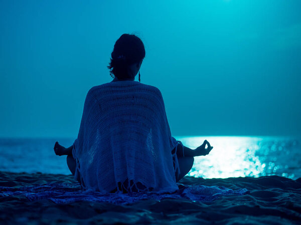 Yoga under full moon over night ocean or sea beach. Young womans meditation
