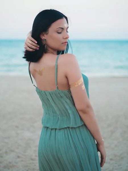 Портрет красивой брюнетки на пляже с татуировками на руках, спине и лбу. Цыганский стиль бохо, Женщина в длинном зеленом платье . — стоковое фото