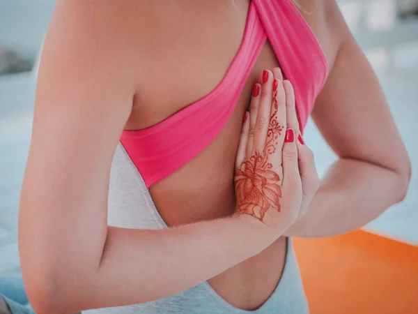 Фітнес-леді в спортивному одязі практикує йогу з іменем, медитує, розслабляє сидячи в молитовному положенні на морському океані, близько до води. Руки з татуюванням мейнді — стокове фото
