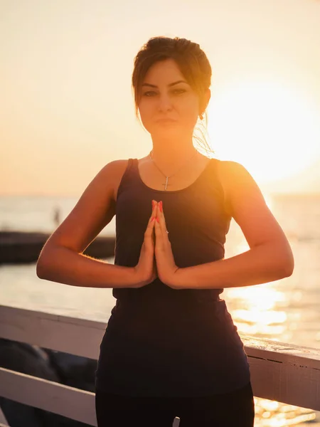 Ritratto di bella donna in abbigliamento sportivo che pratica yoga con namaste, medita, respira, si rilassa seduta in posizione di preghiera sulla spiaggia dell'oceano, vicino all'acqua. Concetto religioso — Foto Stock