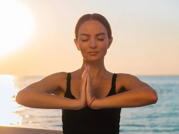 Retrato de mulher bonita em sportswear praticando ioga com namaste, meditando, respirando, relaxando sentado na posição de oração na praia do mar oceano, perto da água. Conceito de religião — Fotografia de Stock