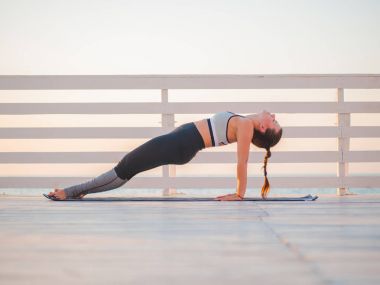 Bir ahşap balkon ya da denize bakan köprü doğada Yoga asana yaparken genç beyaz kadın. Kadının doğada rahatlatıcı okyanus üzerinde pratik yapması. Kız spor giyim.