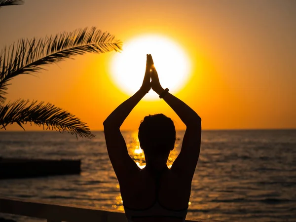 Silhouette di donna in abbigliamento sportivo praticare yoga con namaste, meditare, respirare, rilassarsi seduti in posizione di preghiera sulla spiaggia dell'oceano, vicino all'acqua. Suria namaskar . — Foto Stock