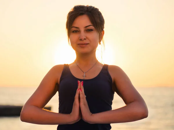 Ritratto di bella donna in abbigliamento sportivo che pratica yoga con namaste, medita, respira, si rilassa seduta in posizione di preghiera sulla spiaggia dell'oceano, vicino all'acqua. Concetto religioso — Foto Stock