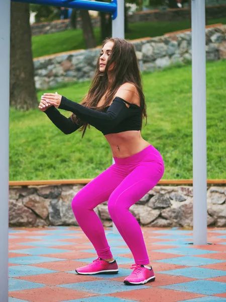 Vacker ung kaukasisk kvinna i fitnesscenter slitage arbetande ute i en park. Kvinna med långt hår och sexig outfit gör sport övningar i fältet atletisk — Stockfoto