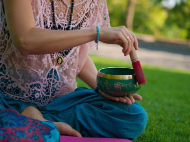 Tibet şarkı kase doğada oynamaya bir kadının elleri. Vintage tarzı. Japa mala, yaz parkta meditasyon yoga mat ile güzel kız.