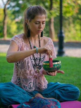Tibet şarkı kase doğada oynamaya bir kadının elleri. Vintage tarzı. Japa mala, yaz parkta meditasyon yoga mat ile güzel kız.