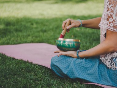Tibet şarkı kase doğada oynamaya bir kadının elleri. Vintage tarzı. Japa mala, yaz parkta meditasyon yoga mat ile güzel kız.