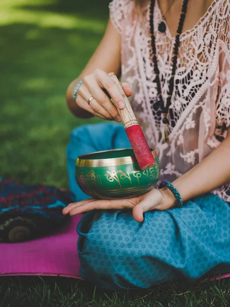 Kezében egy nő játszik a tibeti éneklő bowl, a természetben. Vintage stílusú. Gyönyörű lány japa mala, jóga szőnyeg, meditál a parkban, a nyári. — Stock Fotó