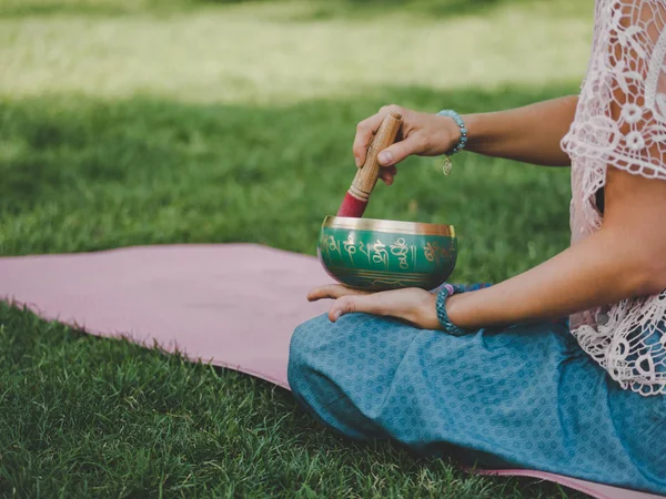 Hände einer Frau, die in der Natur tibetische Klangschalen spielt. Vintage-Stil. schöne Mädchen mit japa mala, Yogamatte meditieren im Park im Sommer. — Stockfoto