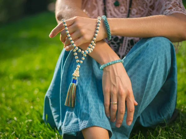 Frau, beleuchtete Hand aus nächster Nähe, zählt malas, Stränge aus Holzperlen, die während Mantra-Meditationen zum Zählen verwendet werden. Buddhismus. Mädchen sitzt im Sommer im Park. — Stockfoto