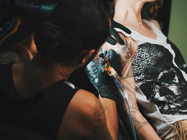 Adam dövme master oluşturma dövme işlemi lambanın altında kadın vücudunda hafif gösteren dreadlocks ile portresi. Salonda, çalışma profesyonel sanatçı görünümü kapatın. — Stok fotoğraf