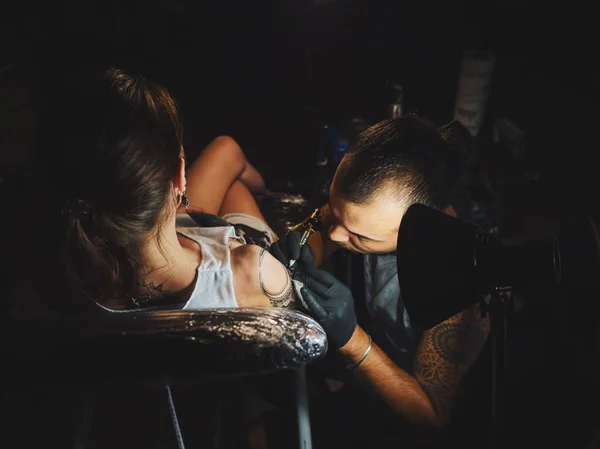 人纹身大师与长发绺显示创作纹身过程对女性的身体，在灯下光的肖像。专业的艺术家在沙龙，工作关闭视图. — 图库照片