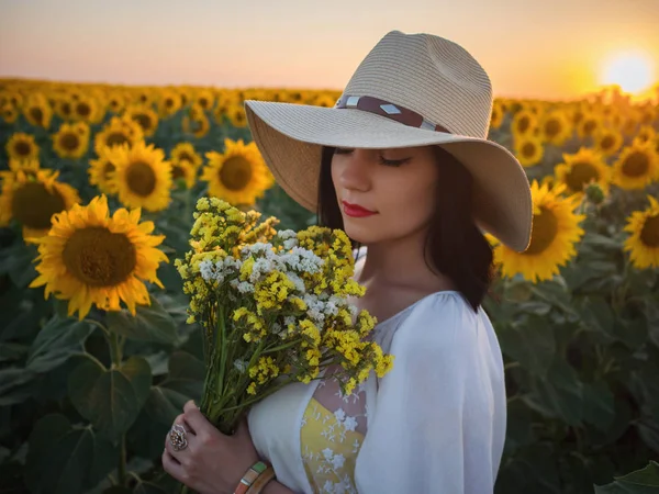 Szczęśliwa Kobieta w Słonecznikowe pole. Dziewczyna lata w kwiat pole wesoły i radosny. Kaukaski panienka w kowbojski kapelusz gospodarstwa Bukiet żółtych kwiatów. Pojęcie kobiecości. — Zdjęcie stockowe