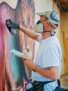 Sokak duvar grafiti sanatçısı resim. Aerosol püskürtülen ilaç şişe duvarının yakınında olan adam. Koruyucu maske renkli aslan çizim genç yetenekli adam.