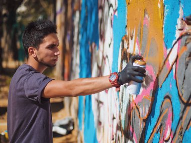 Yakışıklı yetenekli genç çocuk kentsel sokak duvara aerosol sprey ile renkli bir graffiti yapmak. Sinema tonedshot. Yaratıcı sanat. Yan görünüm